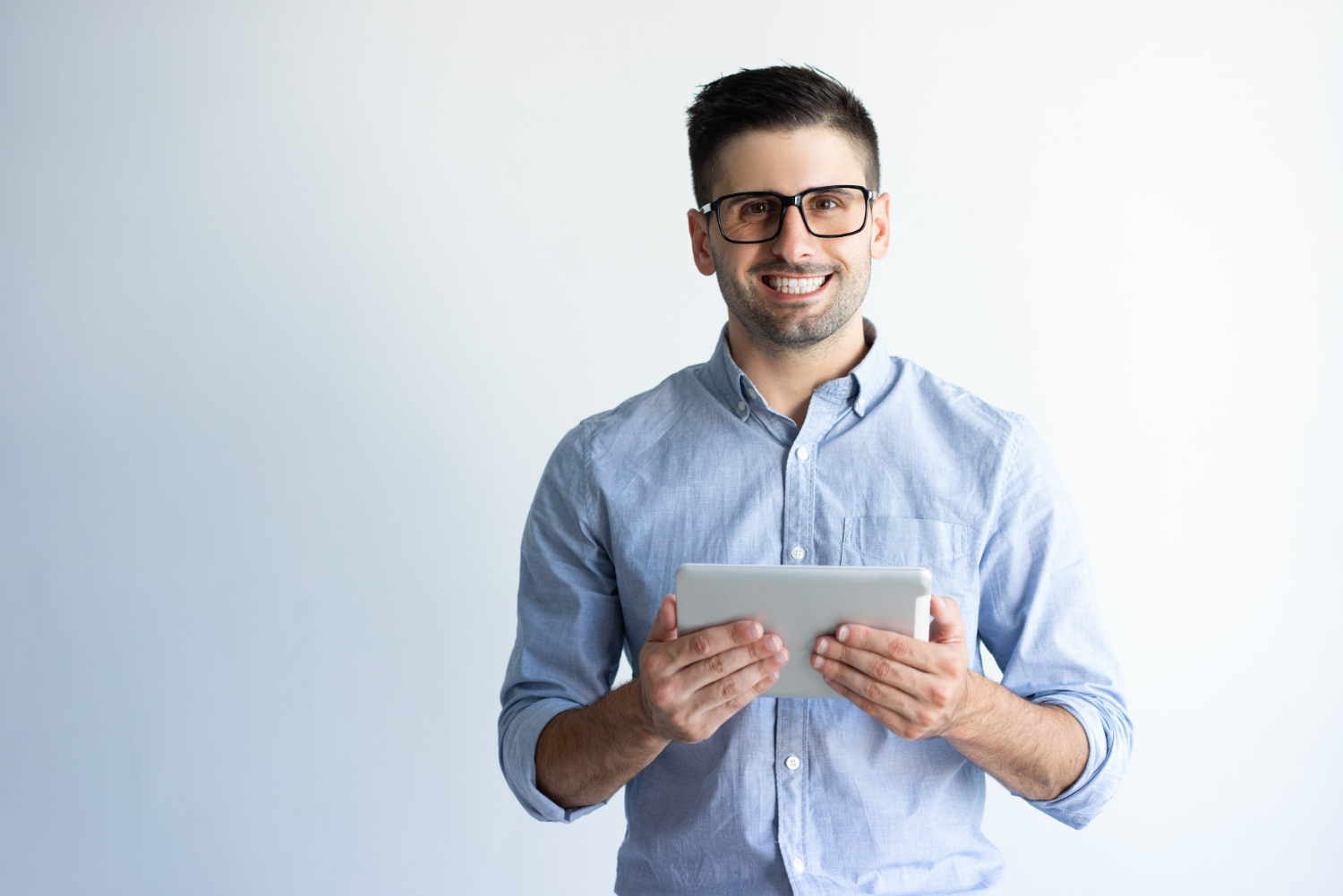 Homem jovem em um fundo branco-cinza, segurando um tablet e sorrindo para frente, dando a ideia de trabalhador de terceirização de TI